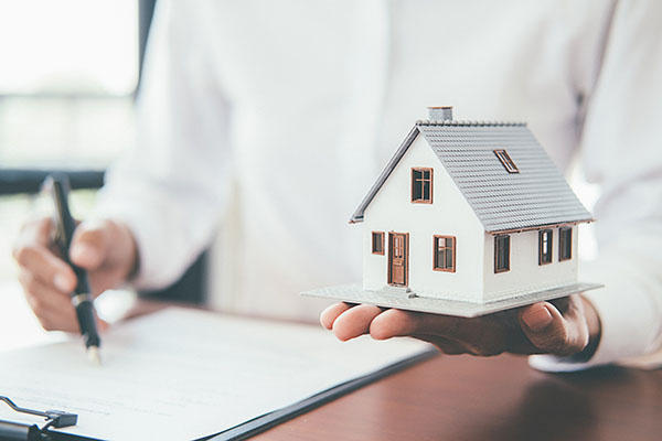 A person holding a model home in their hand, while signing a contract