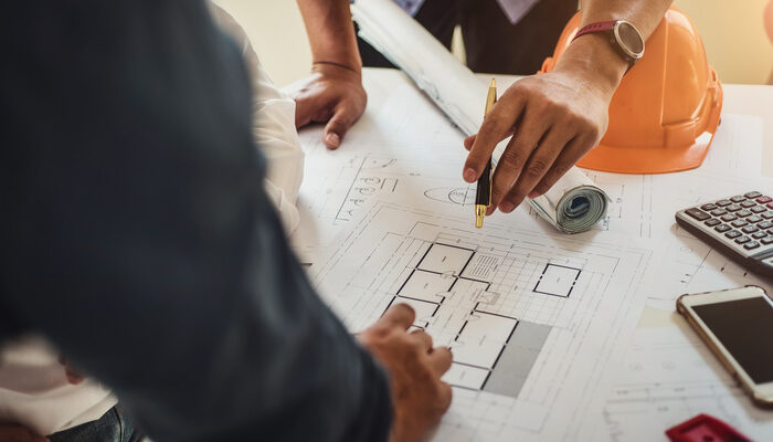 Engineer and general contractor working at a blueprint of house in office for discussing real estate project.
